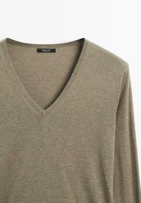 Olivengrüner, weicher Strickpullover; V-Ausschnitt-Design mit langen Ärmeln. Etikett im Kragen sichtbar, nahtlose Textur. Leichtes Material.