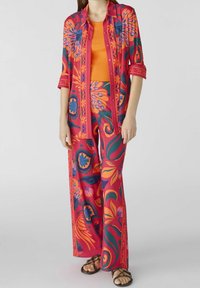 Tenue en deux pièces composée d'une chemise à motif floral vif avec des manches retroussées et un pantalon ample assorti dans des teintes de rose et d'orange.