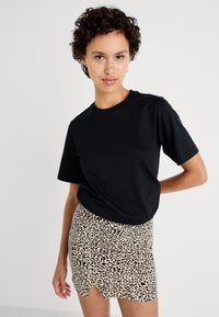 Svart bomulls t-skjorte med korte ermer, parret med et beige leopardmønstret miniskjørt med en frontslitt. Glatt tekstur gjennom hele.