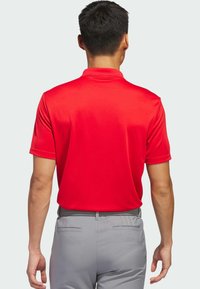 Rød polo T-shirt med korte ærmer, glat tekstur og flad krave. Sammen med grå bukser, der har et vævet bælte og sidelommer.