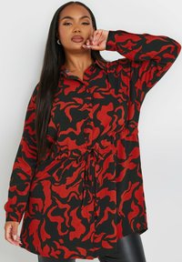 Vestito camicia con motivo rosso e nero, maniche lunghe, chiusura con bottoni e vita cintrata, caratterizzato da una vestibilità morbida e un orlo curvo.