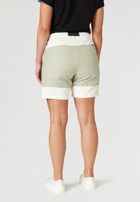 Helle graue Shorts mit einem weißen Bund und Bündchen, im entspannten Schnitt und mit elastischem Bund. Getragen mit weißen Sneakers.