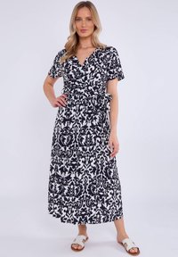 Maxi dress in black and white, featuring a wrap design, short sleeves, and a patterned texture with a tied waist. Paired with white sandals.