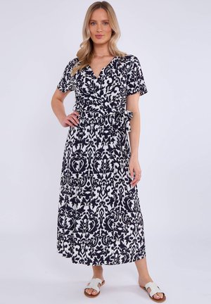 Maxi dress in black and white, featuring a wrap design, short sleeves, and a patterned texture with a tied waist. Paired with white sandals.