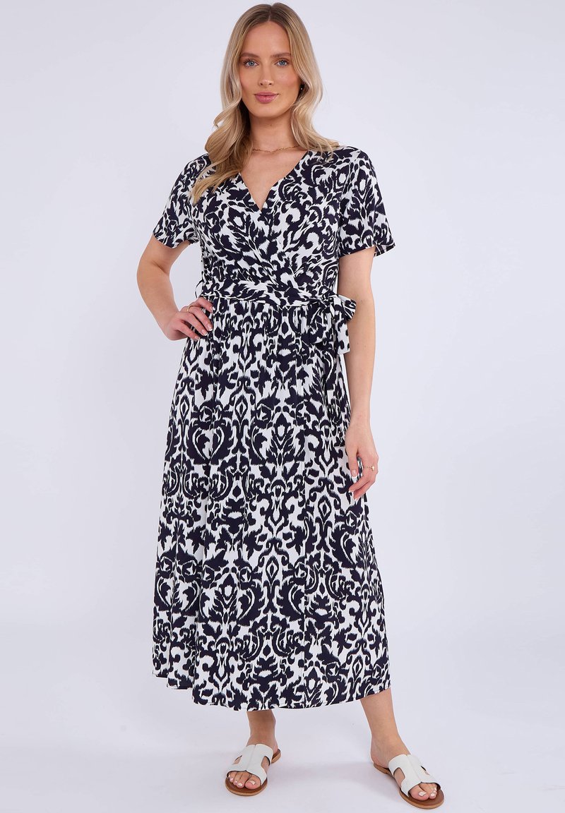 Maxi dress in black and white, featuring a wrap design, short sleeves, and a patterned texture with a tied waist. Paired with white sandals.