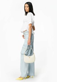 Blusa bianca con maniche a palloncino, pantaloni cargo larghi di un azzurro chiaro, scarpe gialle a punta, borsa color crema con hardware dorato e forma curva.