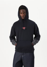 Hoodie marine avec des manches grises, poche frontale, et un design graphique central en rouge. Tissu doux avec des poignets et un ourlet côtelés.