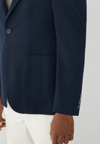 Mornaricno plavi sako s teksturiranom tkaninom, ravnim reverima, lijevim džepom na prsima i detaljem s četiri gumba na manžetama. Slim fit dizajn s krojenom strukturom.
