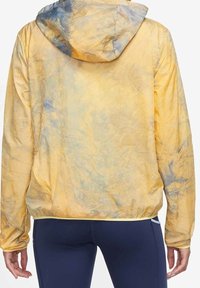 Chaqueta ligera de tie-dye en amarillo pastel con acentos azules, que presenta una capucha y puños fruncidos, textura suave y corte relajado.