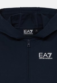 Sudadera con cremallera azul marino hecha de un tejido suave, con cremallera frontal, capucha forrada y un logo EA7 bordado en blanco en el pecho.