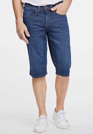 Shorts en denim bleu foncé avec une coupe droite, dotés de poches avant et de détails de couture discrets, associés à des baskets blanches.