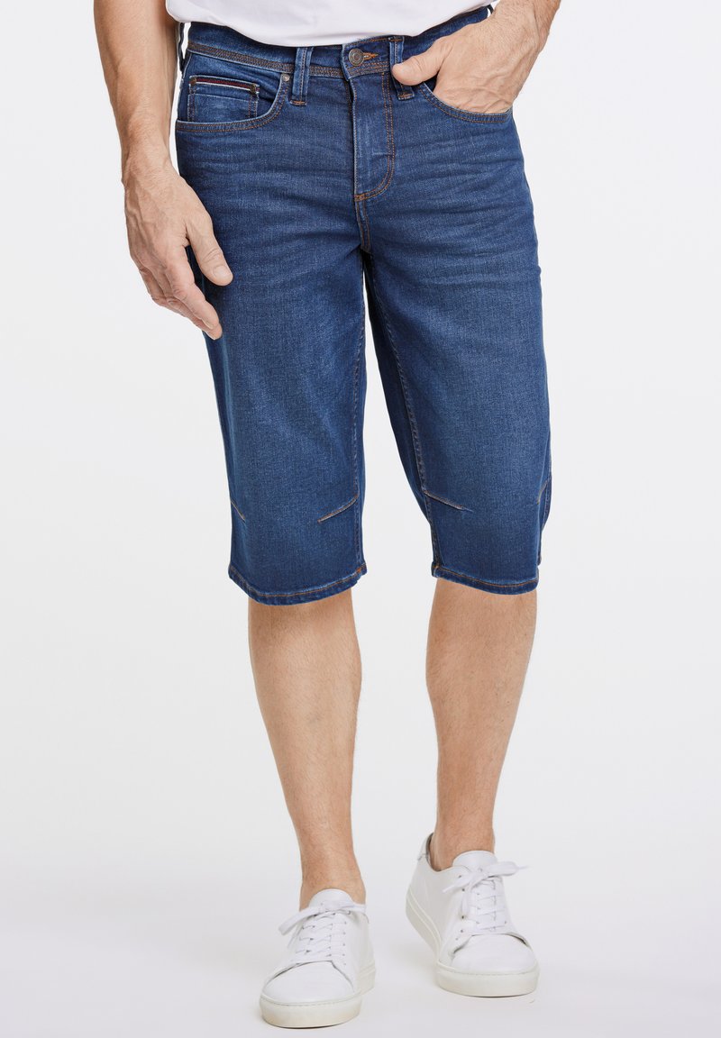 Shorts de mezclilla en azul oscuro con corte recto, que presentan bolsillos frontales y sutiles detalles de costura, combinados con zapatillas blancas.