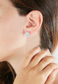 Orecchini in tonalità argento a forma di pera, circondati da piccole pietre rotonde, con una finitura lucida e dettagli testurizzati.