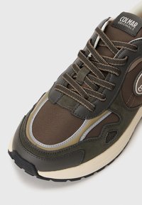 Rudi sportbačiai, pagaminti iš zomšos ir tinklinės medžiagos, su siauru dizainu, tekstūruotomis raištelėmis ir kontrastingomis pilkomis detalėmis.