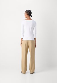 Top blanco de manga larga con escote amplio, combinado con pantalones sueltos de color beige. Tela suave, diseño limpio y sin patrones visibles.
