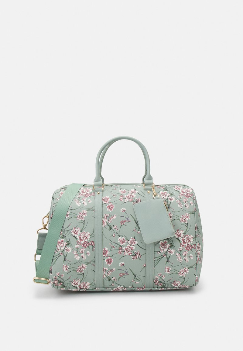 Bolsa de viaje floral verde hecha de material suave. Cuenta con herrajes dorados, doble asa en la parte superior, correa removible y una etiqueta de equipaje.
