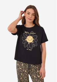 Zwarte katoenen t-shirt met korte mouwen, voorzien van een gele lachende zon en bloemenontwerp, vergezeld van de tekst "Altijd Blij, Meneer Blij."