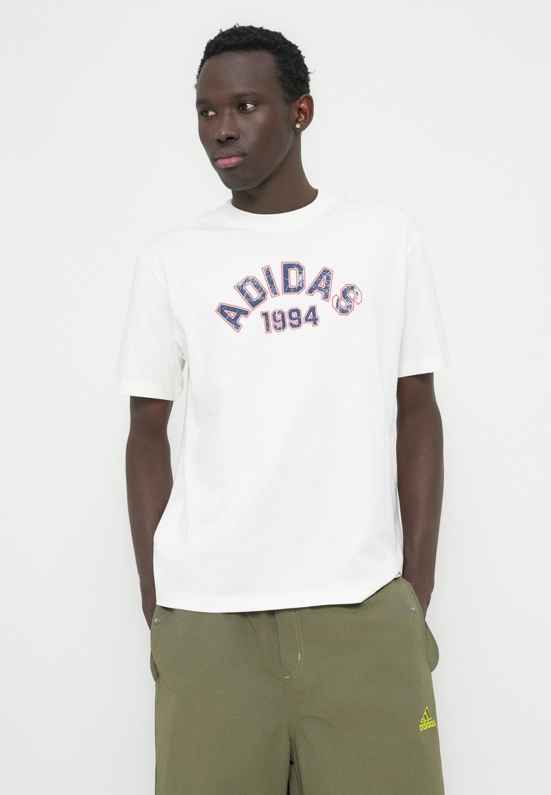 T-shirt en coton blanc avec logo Adidas rouge et bleu accompagné de "1994" en dessous, col rond, manches courtes et coupe décontractée.