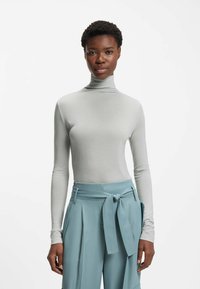 Light gray long-sleeve turtleneck top paired with high-waisted, light blue pleated trousers featuring a tied waist detail. Smooth texture.