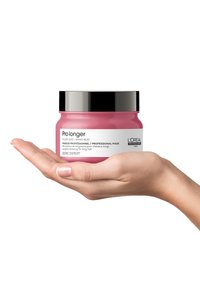Rosa hårmask i en rund burk med ett svart lock. Hand som håller burken, vilket visar dess släta yta och etikettinformation.