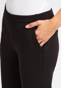 Black trousers with a smooth texture, featuring side pockets and a fitted waist. No visible patterns or hardware details.