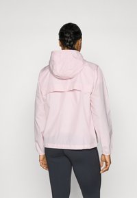 Light pink hooded jacket with elastic cuffs and a back vent. Shiny, smooth material with a relaxed fit. No visible pockets, simple design.