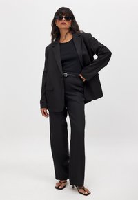 Musthaving mustriga jakk, millele on paigutatud kõhn must topp ja mustad laiad püksid. Aksessuaarideks on mustad prillid ja peen vöö.