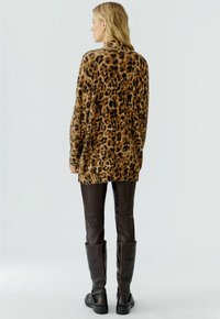 Leren trui met luipaardprint en hoge kraag, lange mouwen en een relaxte pasvorm, gecombineerd met bruin leren skinny jeans en hoge laarzen.