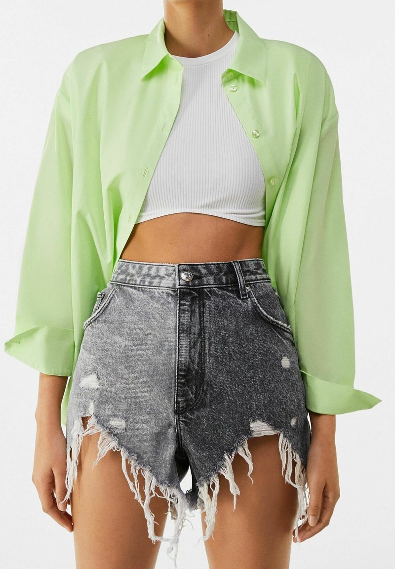 Camisa verde lima, semi-translúcida, abotonada, sobre un crop top blanco con canalé; combinada con pantalones cortos de mezclilla negros de tiro alto con dobladillo deshilachado y desgastado.