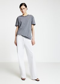 Gray short-sleeve t-shirt with scattered embellishments, paired with loose-fitting white trousers and black sandals on a neutral background.