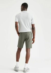 Polo grigio, pantaloni corti verde oliva con due tasche posteriori e calzini bianchi abbinati a scarpe sportive grigie. Sfondo neutro.
