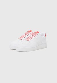 Vita sneakers med röd- och vitrandiga snören. Slät läderövre, perforerad tåbox, solid vit gummisula och röda detaljer på hälen.