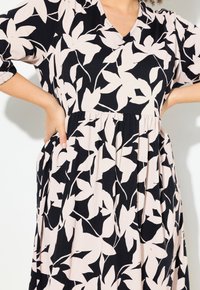 Schwarzes Kleid mit blassrosa Blattmuster, V-Ausschnitt, dreiviertel Ärmel und geraffter Taille. Hergestellt aus leichtem, strukturiertem Stoff.