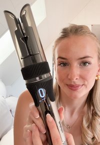 Hiustyökalulla, jossa on tyylikäs metallipinta, musta teksturoitu pito, digitaalinäyttö ja kaksipaikkainen kiharrinpäiden muotoilu.