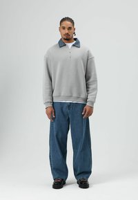 Grijze zip-up sweatshirt met een contrasterende denimkraag, gecombineerd met ruime blauwe jeans en zwarte schoenen. Eenvoudige, ontspannen pasvorm.