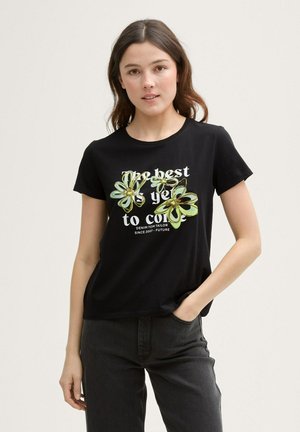 Camiseta negra de manga corta con un diseño gráfico floral en verde y amarillo. El texto dice "Lo mejor está por venir". Textura suave.