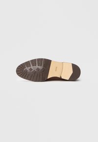 Semelle en caoutchouc brun avec un motif de grip texturé, dotée d'une section de talon de couleur claire et d'un nom de marque en relief. Surface inférieure lisse.