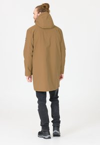 Bruine, capuchon parka met een losse pasvorm, lange mouwen en een rechte snit. Gedragen over zwarte slim jeans en donkere schoenen met gestructureerde zolen.