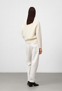Crème kleurige trui met een gestructureerde brei, hoge hals en geribbelde zoom; gecombineerd met loszittende witte broek en zwarte block-heeled laarzen.