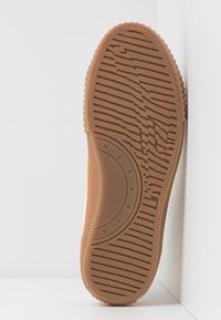 Gummi sål med en strukturell, vågig mönster och cirkulära designelement. Färgen är ljusbrun med djupare horisontella ränder.