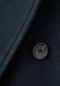 Tessuto di lana di un blu navy scuro con una consistenza liscia, caratterizzato da un bottone rotondo nero con quattro fori. Il tessuto ha una leggera lucentezza.