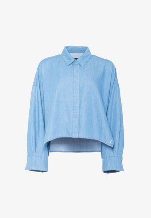 Camisa vaquera azul claro de manga larga y corte cropped, con cuello clásico y tapeta de botones oculta, que presenta puños anchos y un dobladillo ligeramente curvado.