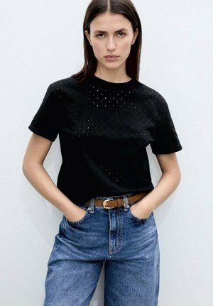 Black short-sleeve T-shirt with textured pattern and small perforations on the front, paired with high-waisted blue denim jeans and a brown belt.