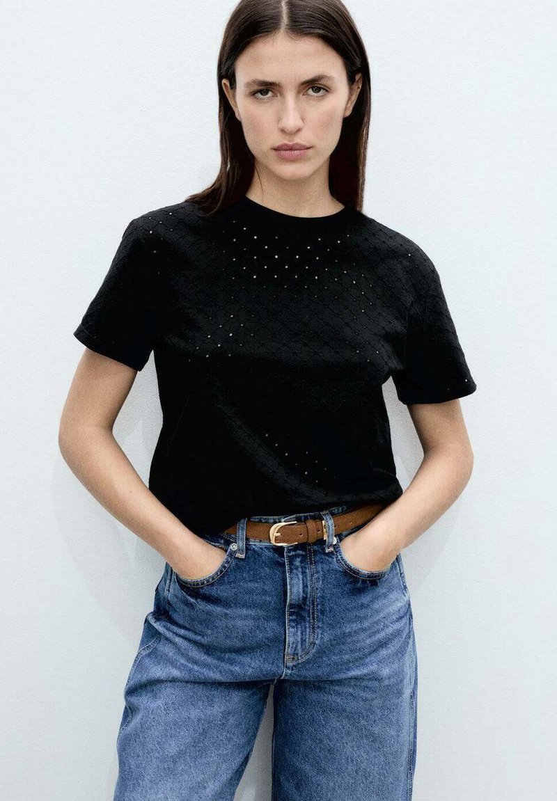Black short-sleeve T-shirt with textured pattern and small perforations on the front, paired with high-waisted blue denim jeans and a brown belt.