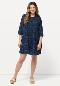 Laiva sininen mekko, jossa on smocked-puku, 3/4-pituiset hihat ja kerroksellinen hame. Sisältää värikkäitä kukkakuoseja kauttaaltaan. Yhdistetty vaaleanruskeisiin alustalojujiin.