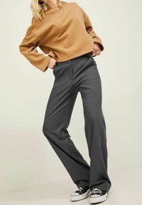 Bruine cropped sweatshirt met brede mouwen, gecombineerd met hoge, lange, grijze broek en zwarte sneakers. Glad stoftexturen.