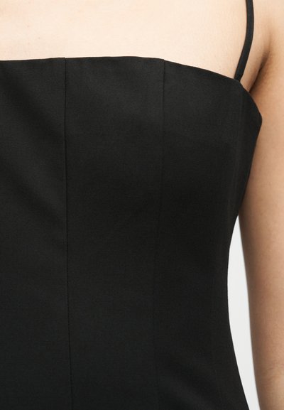 Tuva cilvēka tērps - melna bezroku kleita ar plānām lencītēm un vertikālām šuvēm audumā.