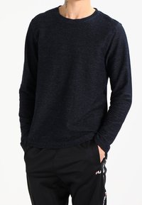 Suéter de manga larga azul marino con cuello redondo, tejido texturizado y silueta ceñida, combinado con pantalones deportivos negros con detalles de logotipo.