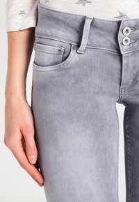 Šedé džínsy z denimu s klasickým designem pěti kapes, zavíráním na dvě knoflíky a hladkou texturou se jemnými detaily vyblednutí.