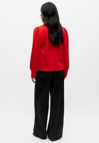 Rotes Langarmshirt mit gepufften Schultern, kombiniert mit hoch taillierten schwarzen weit geschnittenen Hosen. Glattes Material und entspannte Passform.